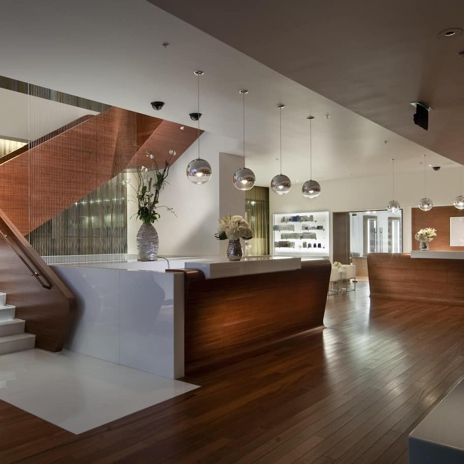 A modern hotel lobby with a wooden reception desk, a staircase, and a large mirror.