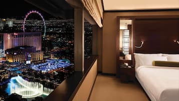 A hotel room with a bed, a nightstand, a lamp, and a view of a cityscape at night including a Ferris wheel and a casino.