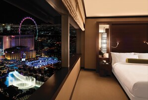 Habitación de hotel con una cama, una mesita de noche, una lámpara y vistas nocturnas de la ciudad que incluyen una noria y un casino.