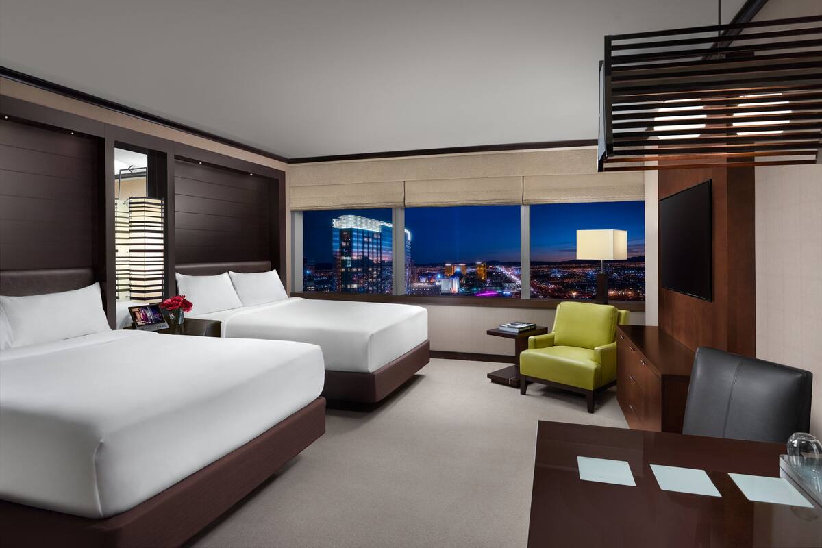 Habitación de hotel con dos camas, un escritorio, una silla, un televisor y vistas a la ciudad.