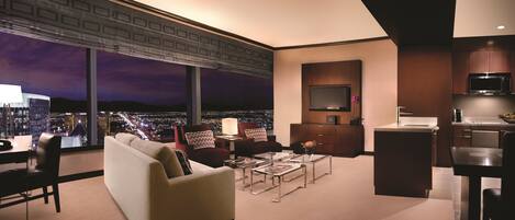 A modern living room with a sofa, armchairs, a coffee table, and a TV. There's a city view through large windows.