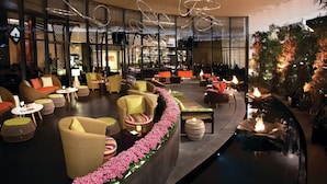 A modern lounge area with wicker furniture, a central fire feature, and a glass wall offering views of the interior. - Vdara Hotel & Spa at ARIA Las Vegas (Las Vegas)