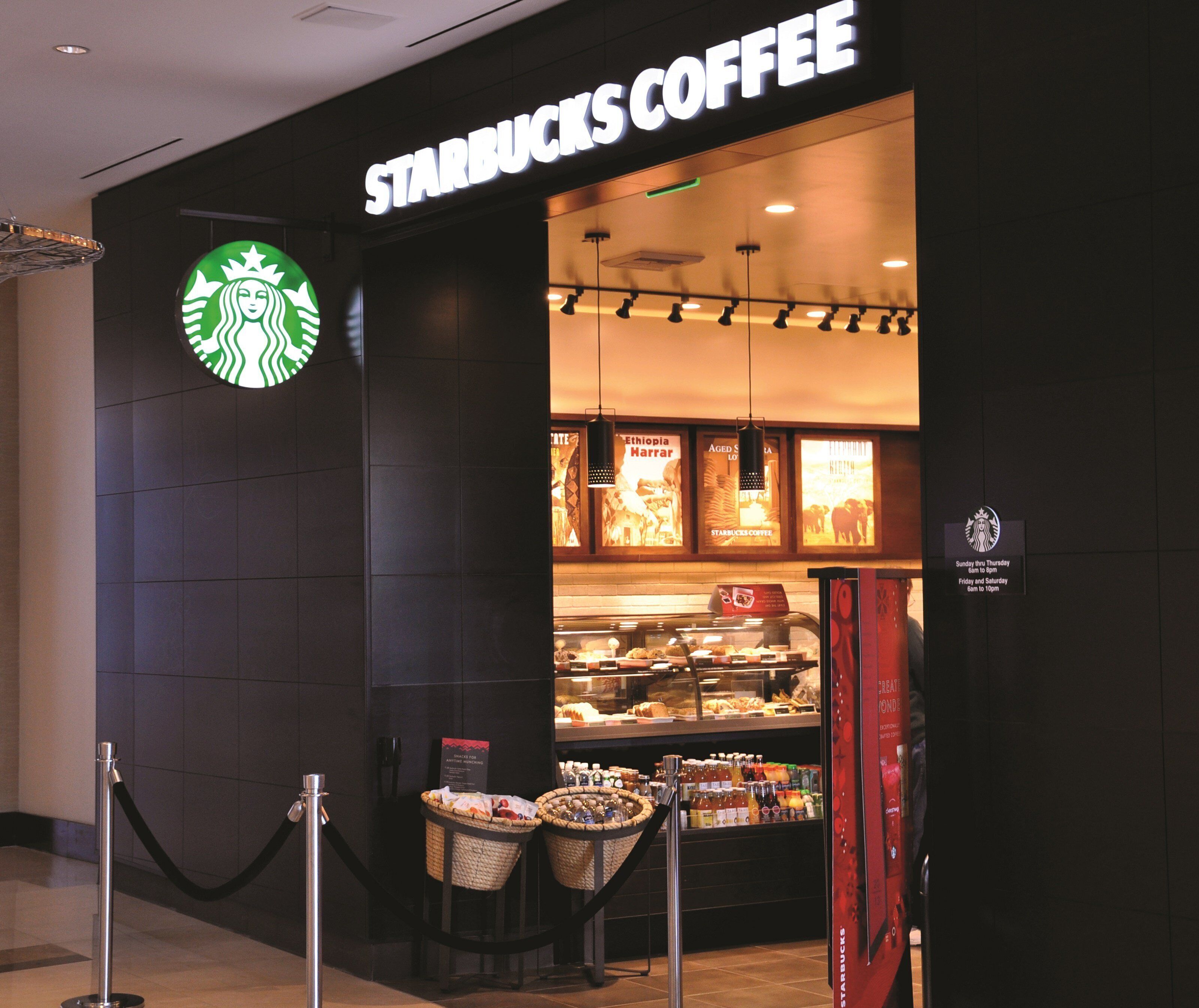 A Starbucks Coffee store with a prominent logo, a display case with various items, and a sign indicating operating hours.