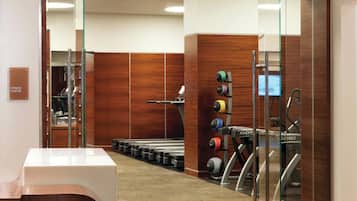 Un gimnasio con equipamiento de ejercicio, cinta de correr y una barra de pesas fijada a la pared.