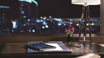 A desk with a tablet, a pen, glasses, and a vase with flowers.
