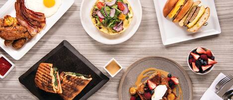 A breakfast spread with eggs, bacon, toast, and fruit on a wooden table.