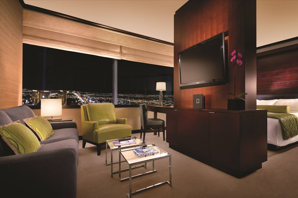 Habitación de hotel moderna con vistas a la ciudad, un escritorio, una cama y un área de descanso.