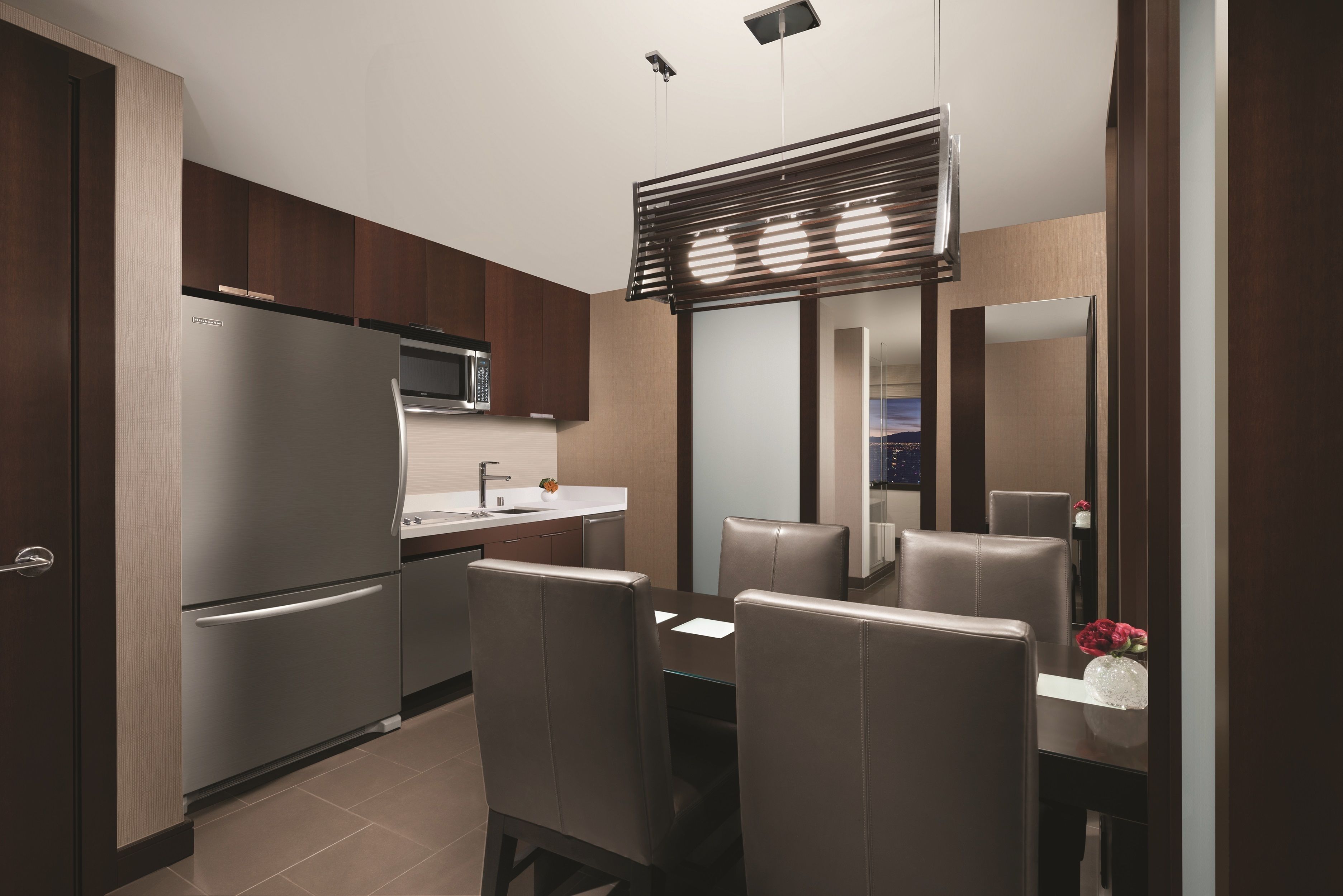 A modern kitchen with a refrigerator, microwave, and dining area with chairs and a table.