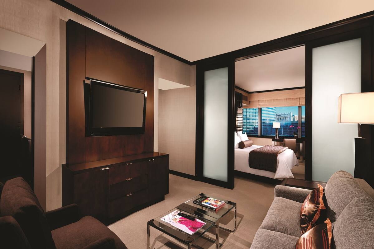 Habitación de hotel con una televisión de pantalla plana grande, una cama con vistas a la ciudad, un escritorio con lámpara y un sofá.