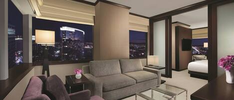 A modern hotel room with a city view, a sofa, a chair, a small table, and a bed.