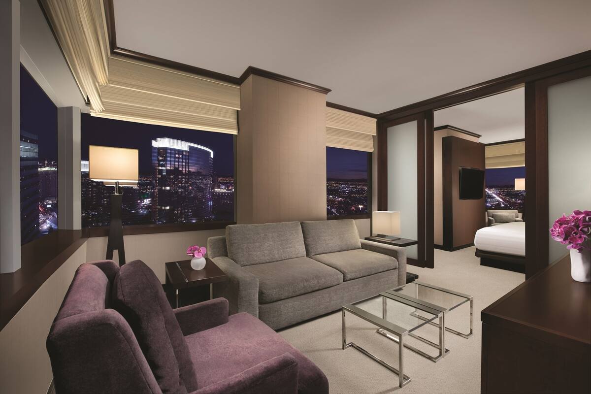 Una habitación de hotel moderna con vista a la ciudad, un sofá, una silla, una mesita y una cama.
