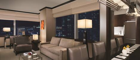 A modern hotel room with a city view, a sofa, a dining table with place settings, and a large window with blinds.