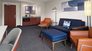 Een hotelkamer met een kitchenette, een bank, een stoel, een tafeltje en een lamp.