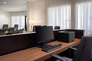 A hotel room with a wooden desk, a computer, a printer, and a chair.