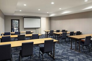 A conference room with multiple tables and chairs, a projector screen, and a large window with a view of trees.