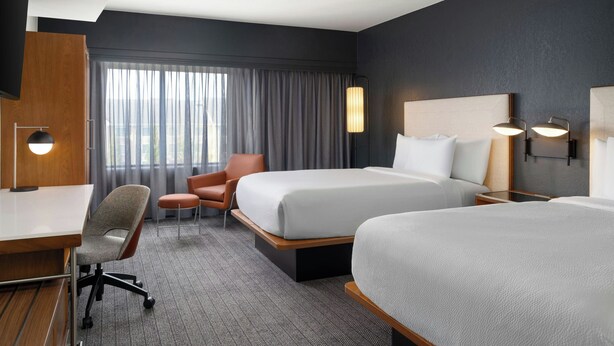 Een hotelkamer met twee bedden, een bureau, een stoel en een groot raam met gordijnen.