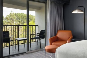 Habitación de hotel con balcón, una silla naranja, una mesita redonda, cama y una lámpara de pie.