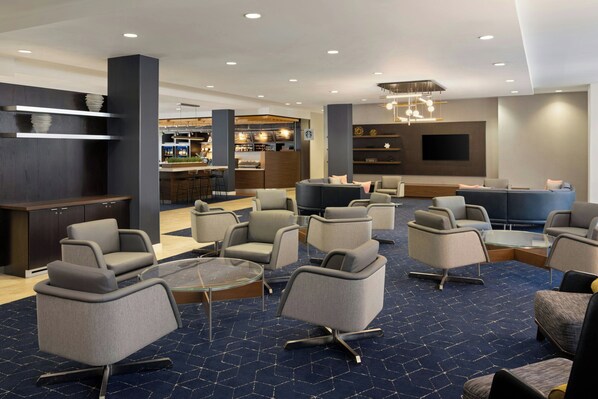 Un hall d’hôtel doté de plusieurs espaces salon, d’un bar et d’un écran de télévision.