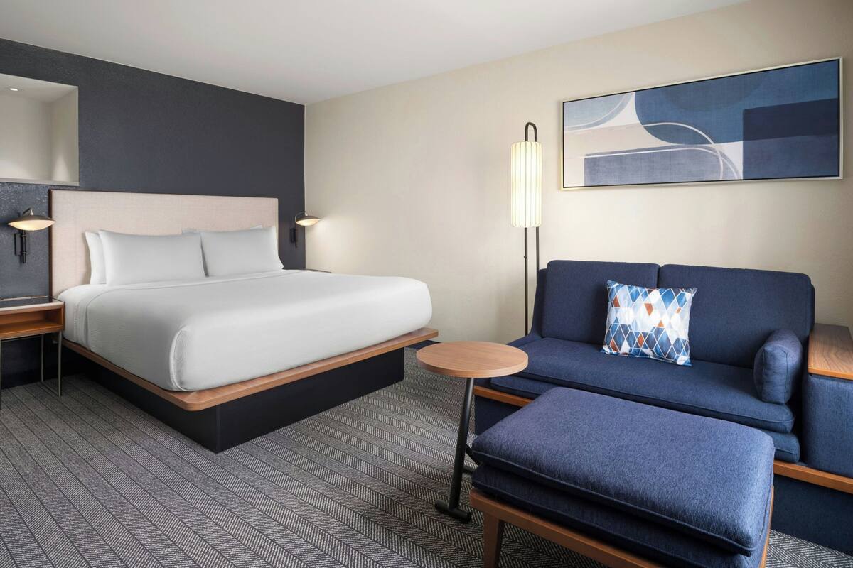 Ein Hotelzimmer mit Bett, Sofa, einem kleinen Tisch, einer Lampe und einem Gemälde an der Wand.
