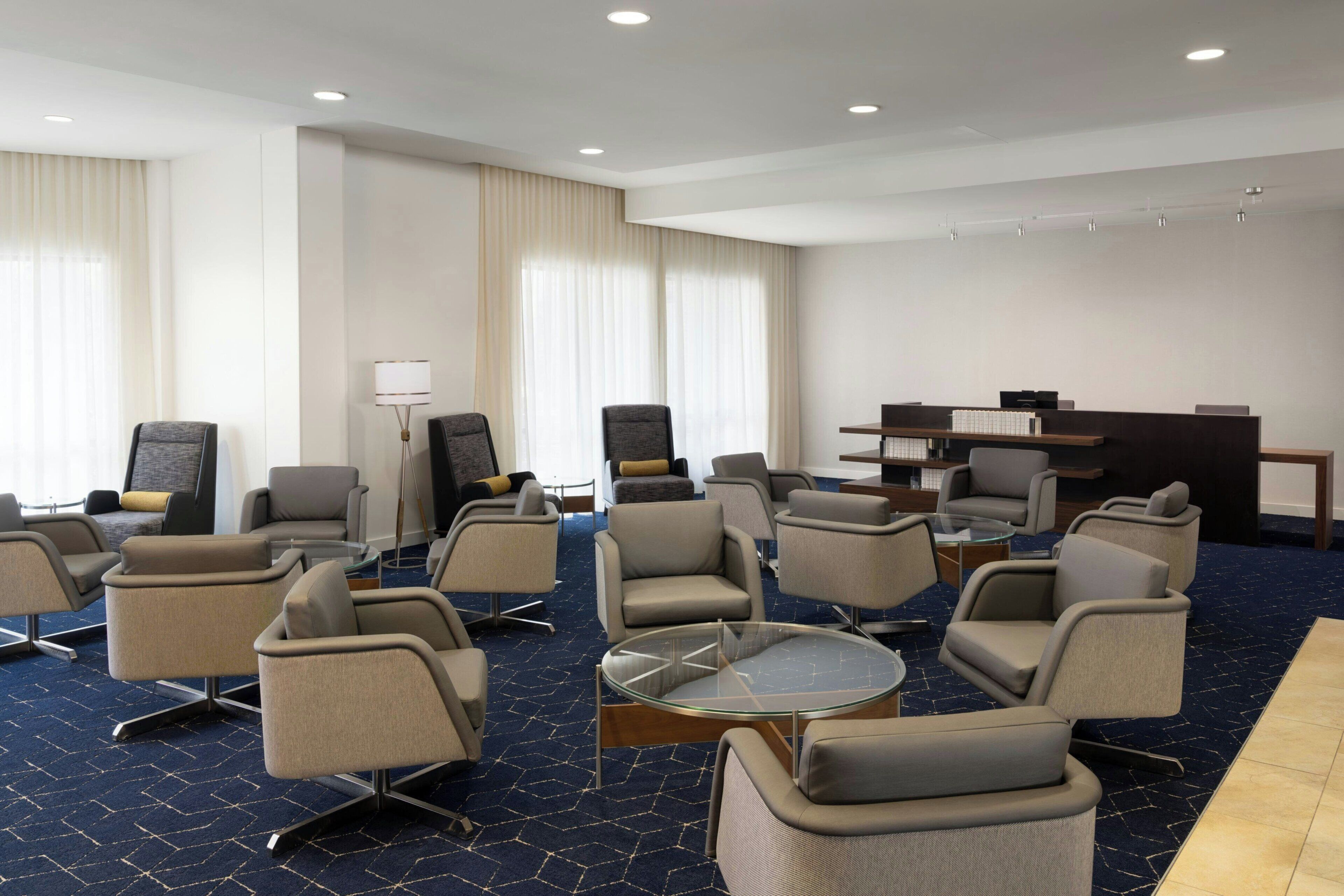 A hotel lobby with multiple seating areas, a reception desk, and a large window with curtains.