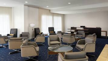 A hotel lobby with multiple seating areas, a reception desk, and a large window with curtains.