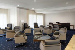 Un hall d’hôtel doté de plusieurs espaces salon, d’un comptoir d’accueil et d’une grande fenêtre avec des rideaux.