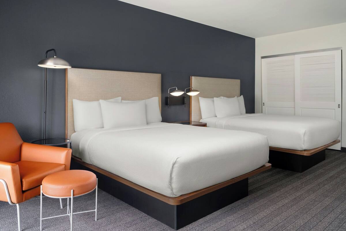Ein Hotelzimmer mit zwei Betten, einem Sessel, einer Lampe und einem Kleiderschrank.