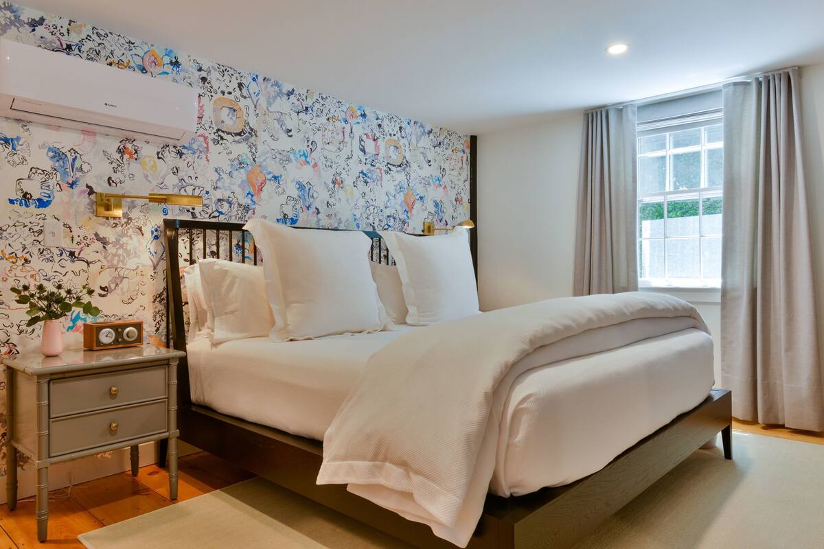 A bedroom with a bed, bedside table, and a wall with a floral pattern.