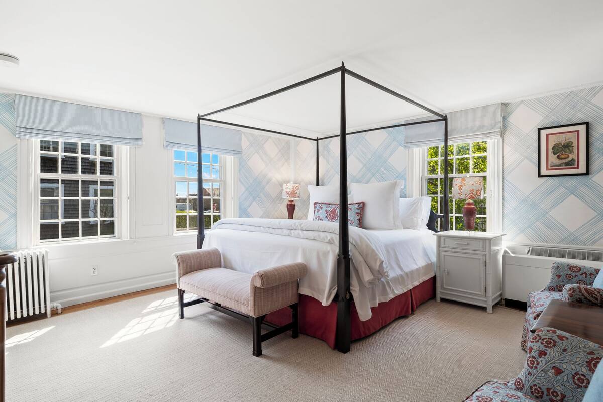 A four-poster canopy bed with a red bed skirt, a bedside table, and a chair.