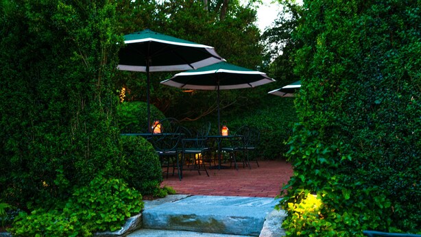 A patio area with stone steps leading up to a table and chairs, surrounded by lush greenery and covered by umbrellas. - Union Street Inn (Nantucket)