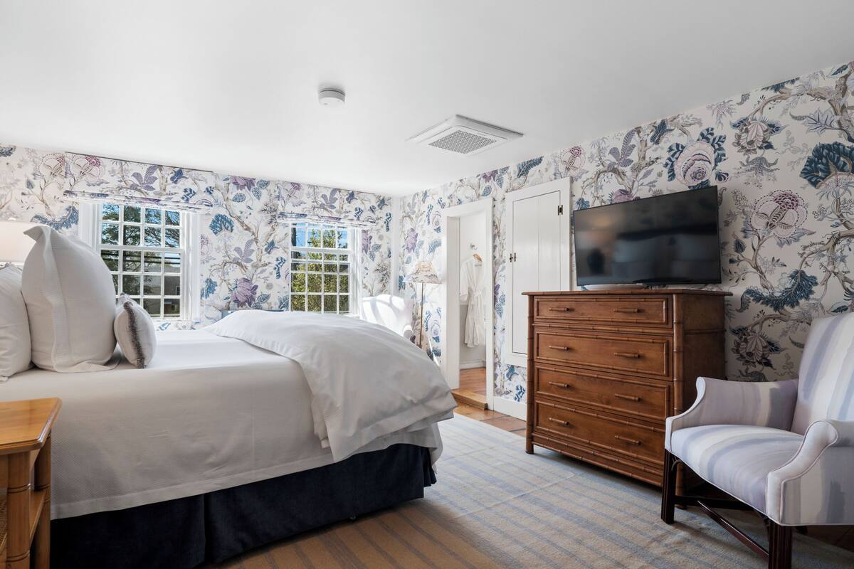 A bedroom with a bed, dresser, chair, and TV.