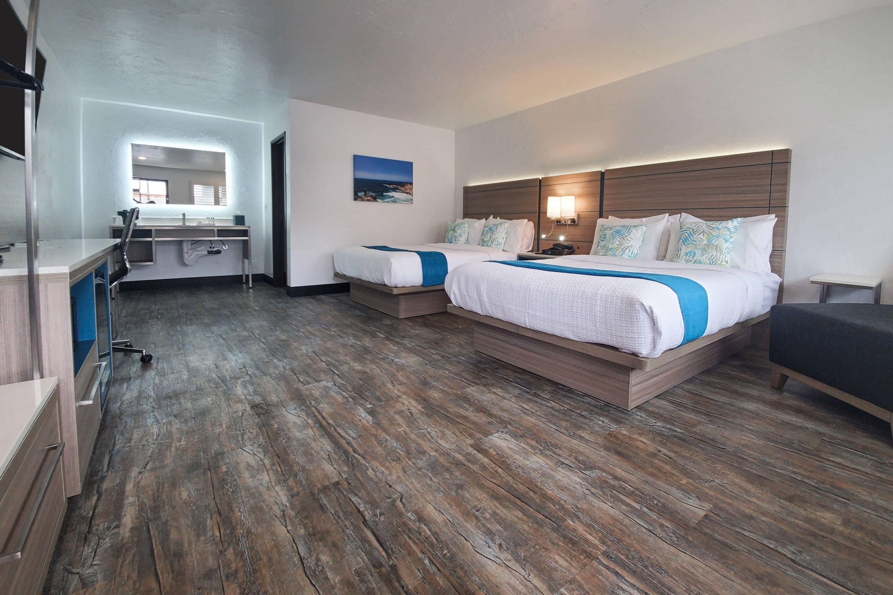 A hotel room with two beds, a desk, a mirror, and a painting on the wall.