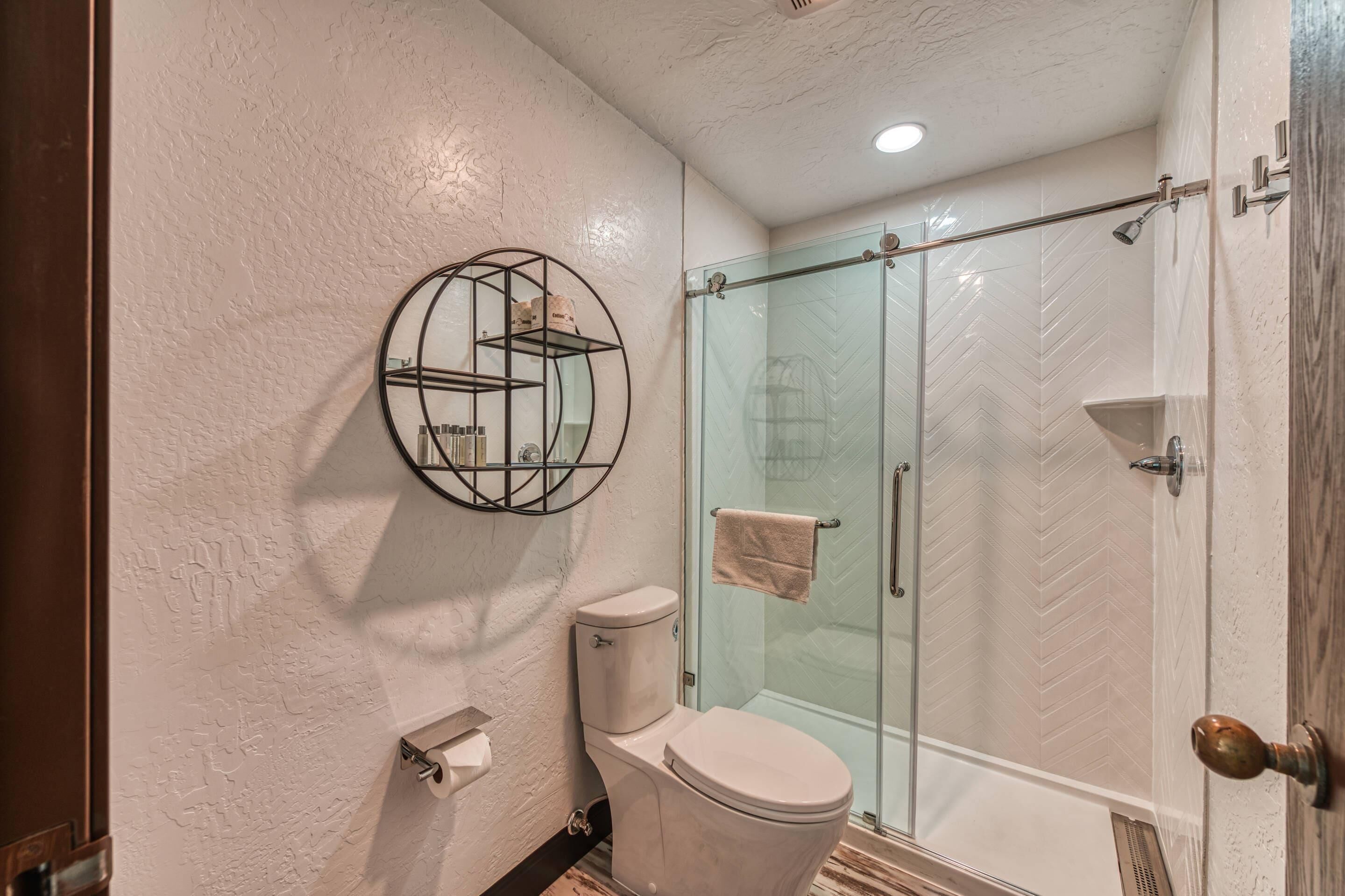 Une salle de bain comprenant des toilettes, une douche à parois de verre et une étagère circulaire où sont rangés les articles de toilette.