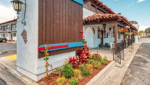 Un bâtiment à la façade en bois brun, ornée d’une bande bleue et rouge, et doté d’un petit jardin avec différentes espèces de plantes.