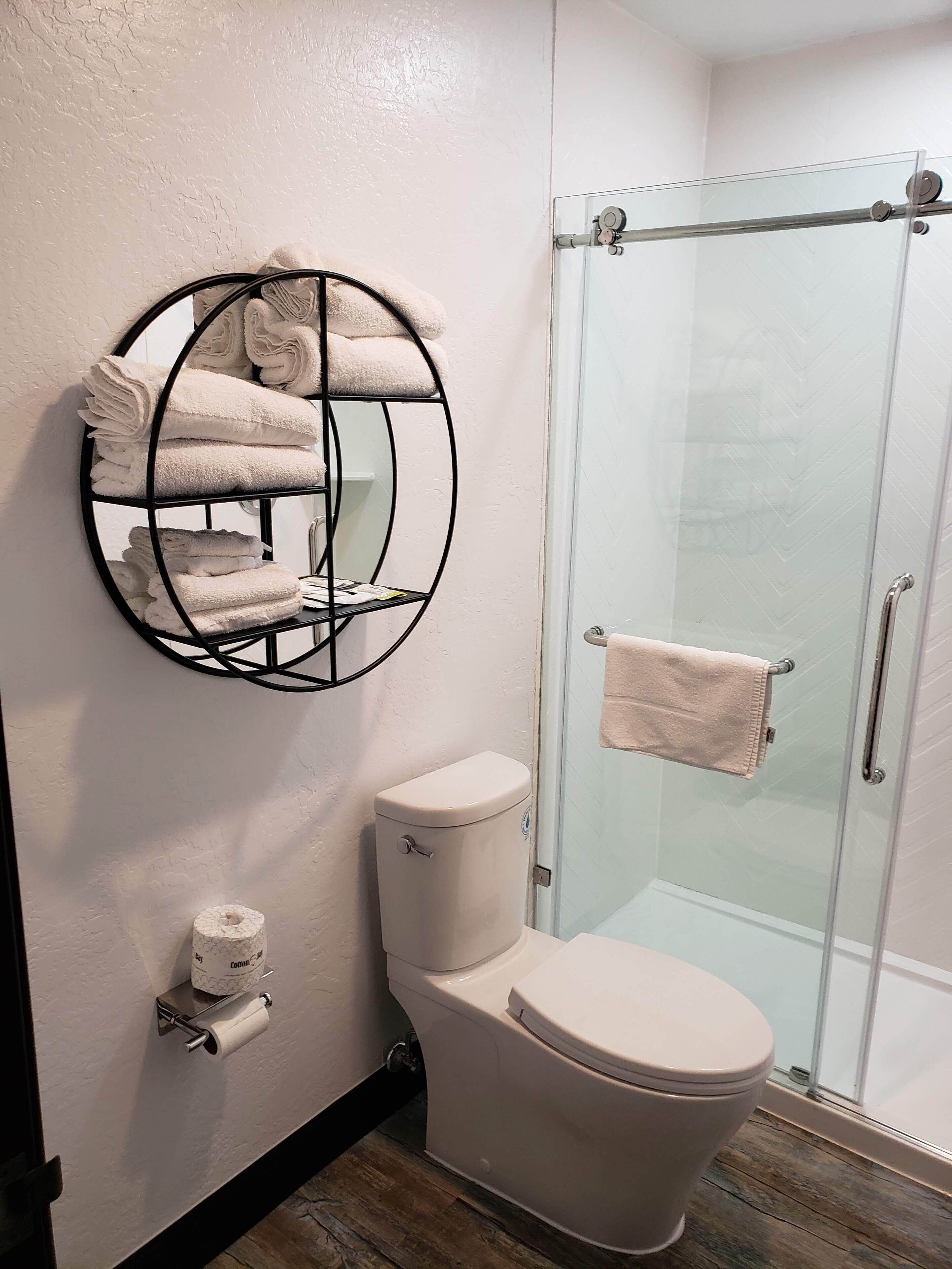 A bathroom with a toilet, a glass shower enclosure, a towel rack with folded towels, and a toilet paper holder.