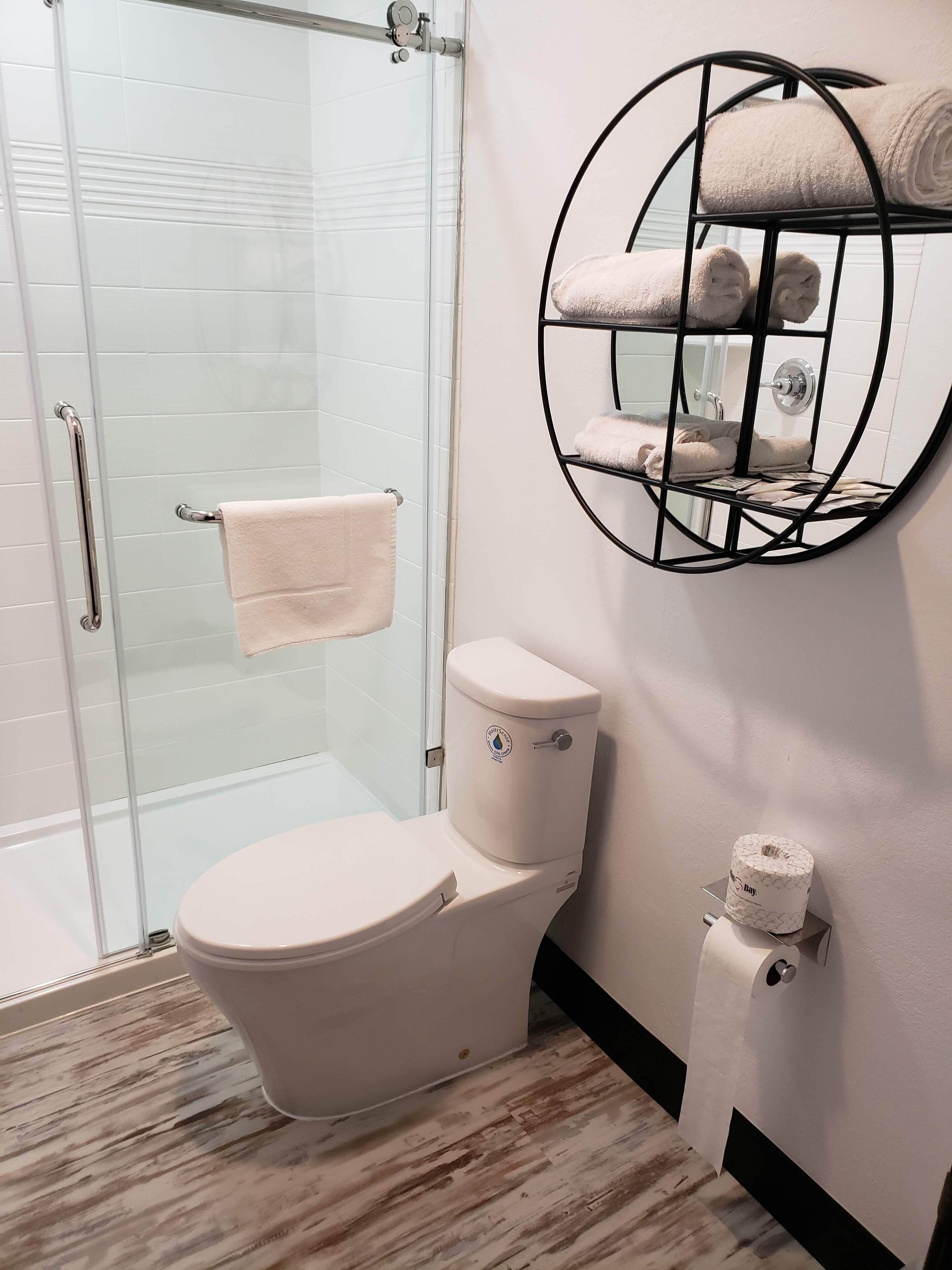 Une salle de bain comprenant des toilettes, une douche à parois de verre, un porte-serviettes avec des serviettes et un porte-rouleau de papier toilette.
