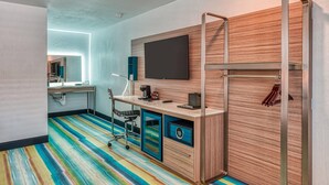Une chambre d’hôtel avec un bureau en bois, un téléviseur à écran plat, une moquette rayée aux couleurs vives, une petite chaise et une armoire avec un miroir.