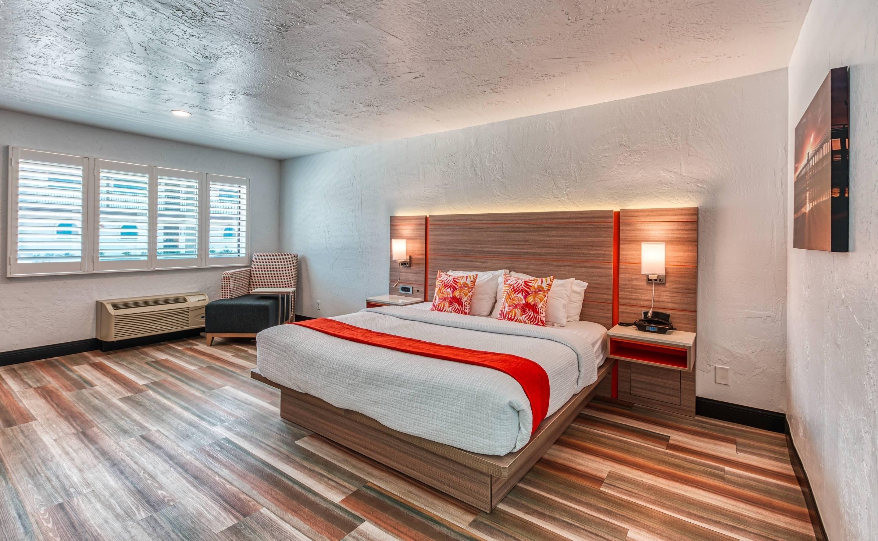 A modern hotel room with a large bed, a chair, a desk, and a heater.