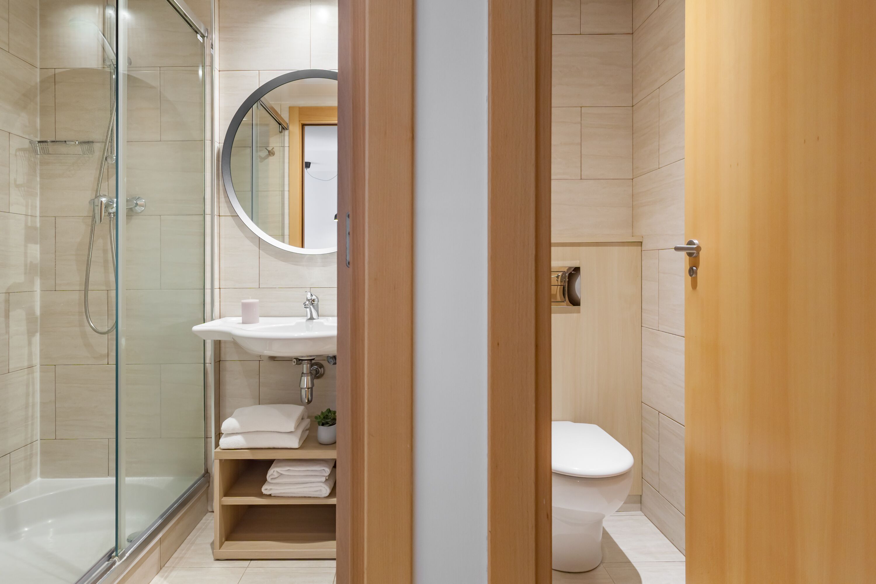A modern bathroom with a glass-enclosed shower, a round mirror, a sink, and a toilet.