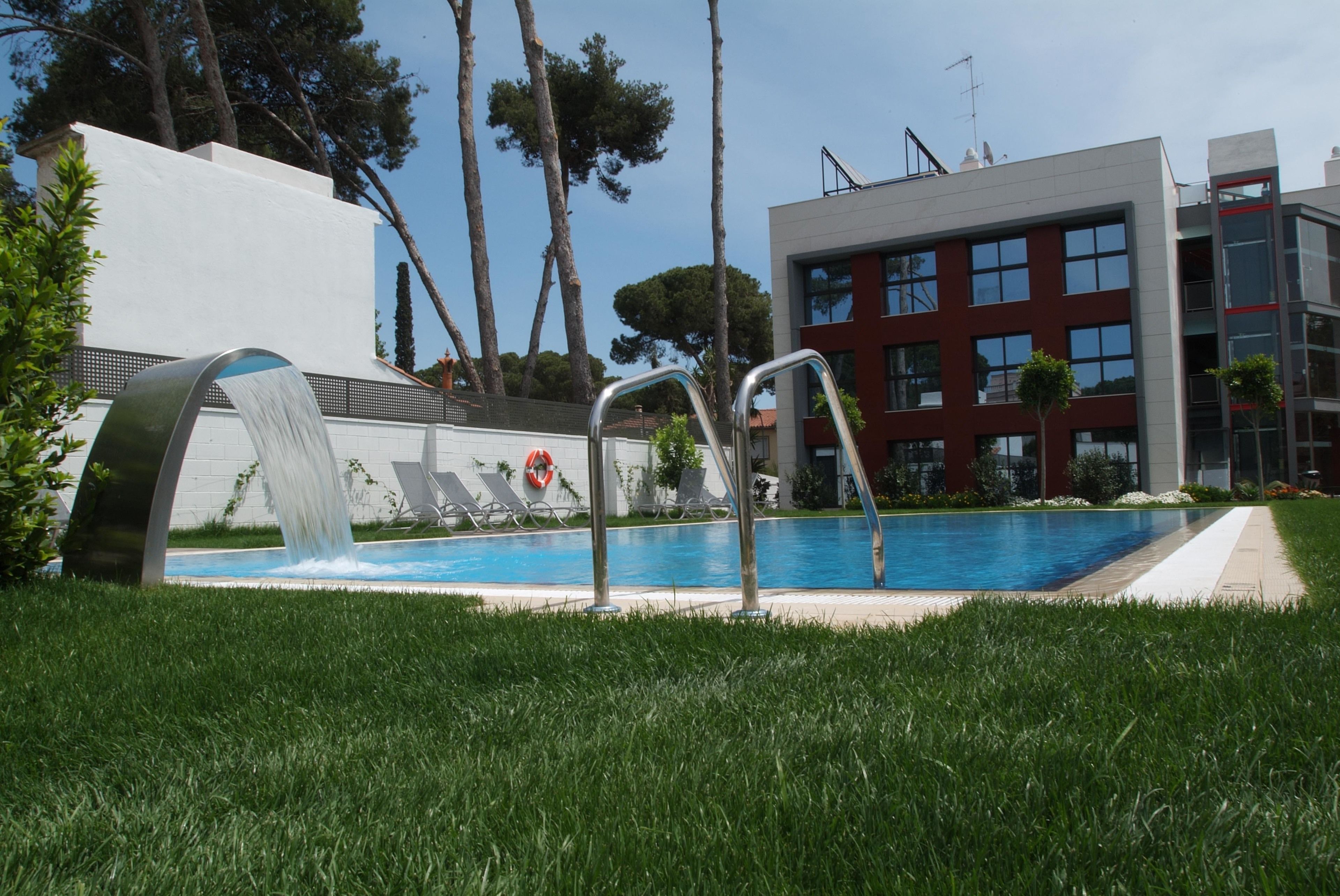 A swimming pool with a modern design, surrounded by a well-maintained lawn and a building with a red facade.