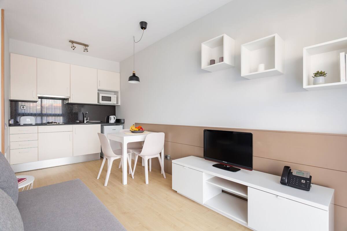 Une cuisine moderne avec des meubles blancs, un four à micro-ondes et un coin repas comprenant une table et des chaises blanches.