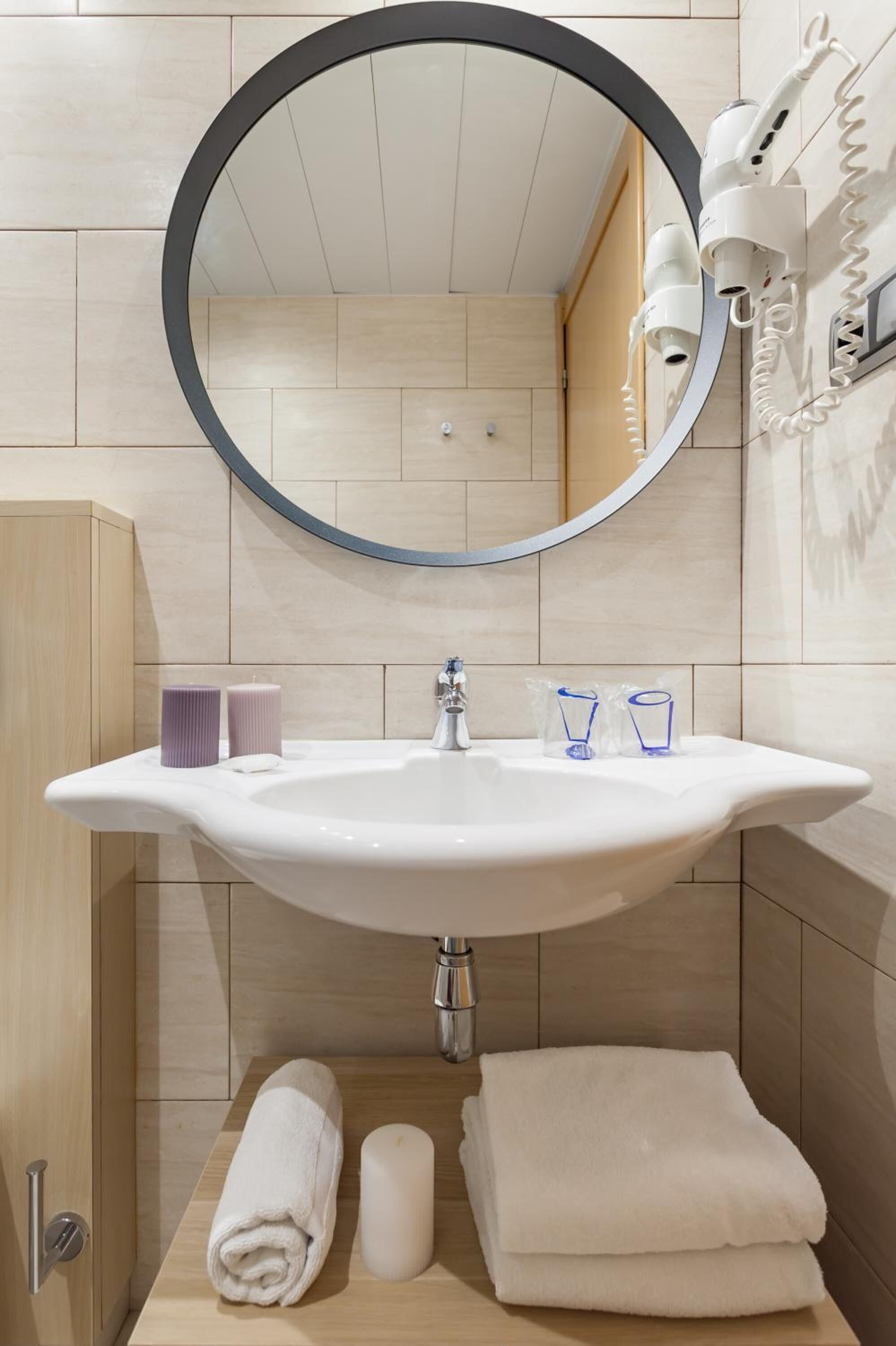 Een badkamer met een witte wastafel, een ronde spiegel en een aan de muur bevestigde haardroger.