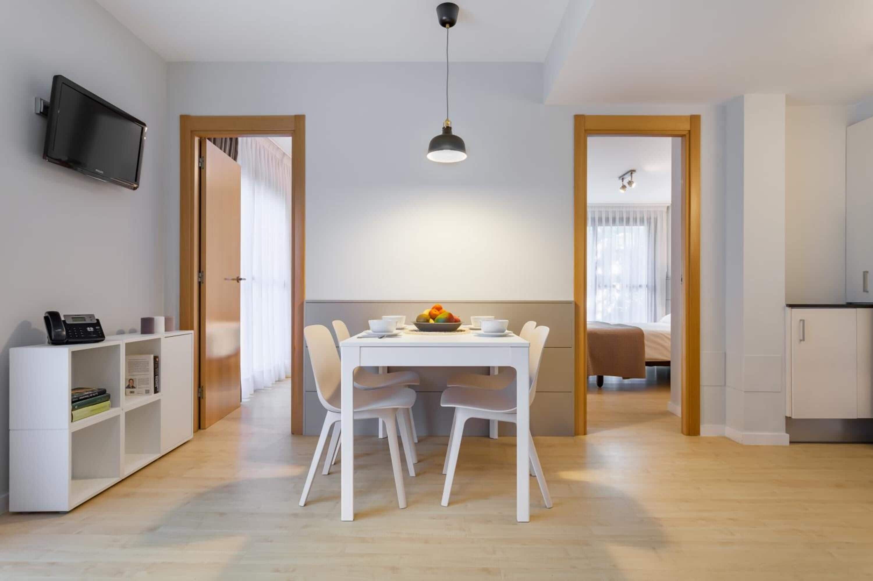 Une pièce moderne et bien éclairée, comprenant une table à manger, des chaises, un téléviseur et une bibliothèque.