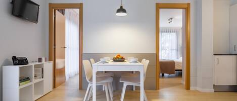 Une pièce moderne et bien éclairée, comprenant une table à manger, des chaises, un téléviseur et une bibliothèque.