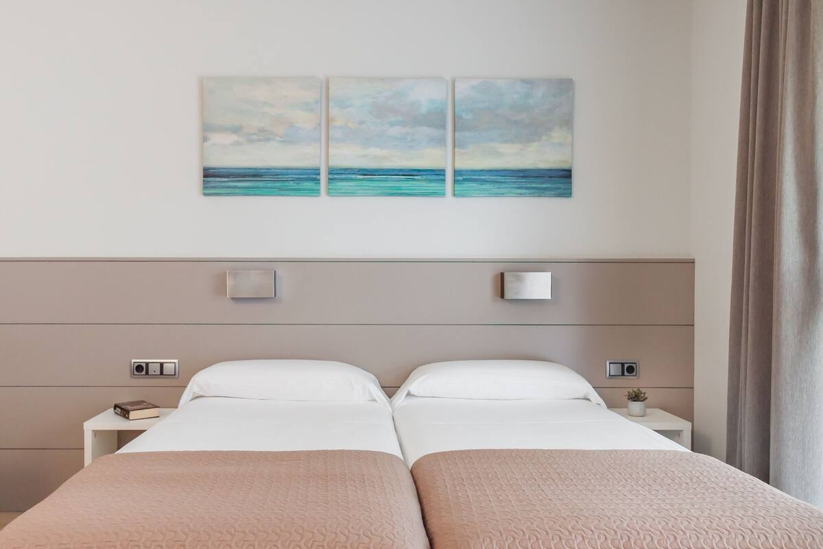 Un lit double avec une tête de lit beige, deux tables de chevet et un luminaire fixé au mur.