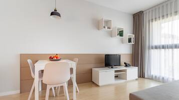A modern hotel room with a bed, a desk with a computer, a chair, a small table with fruit, and a TV.
