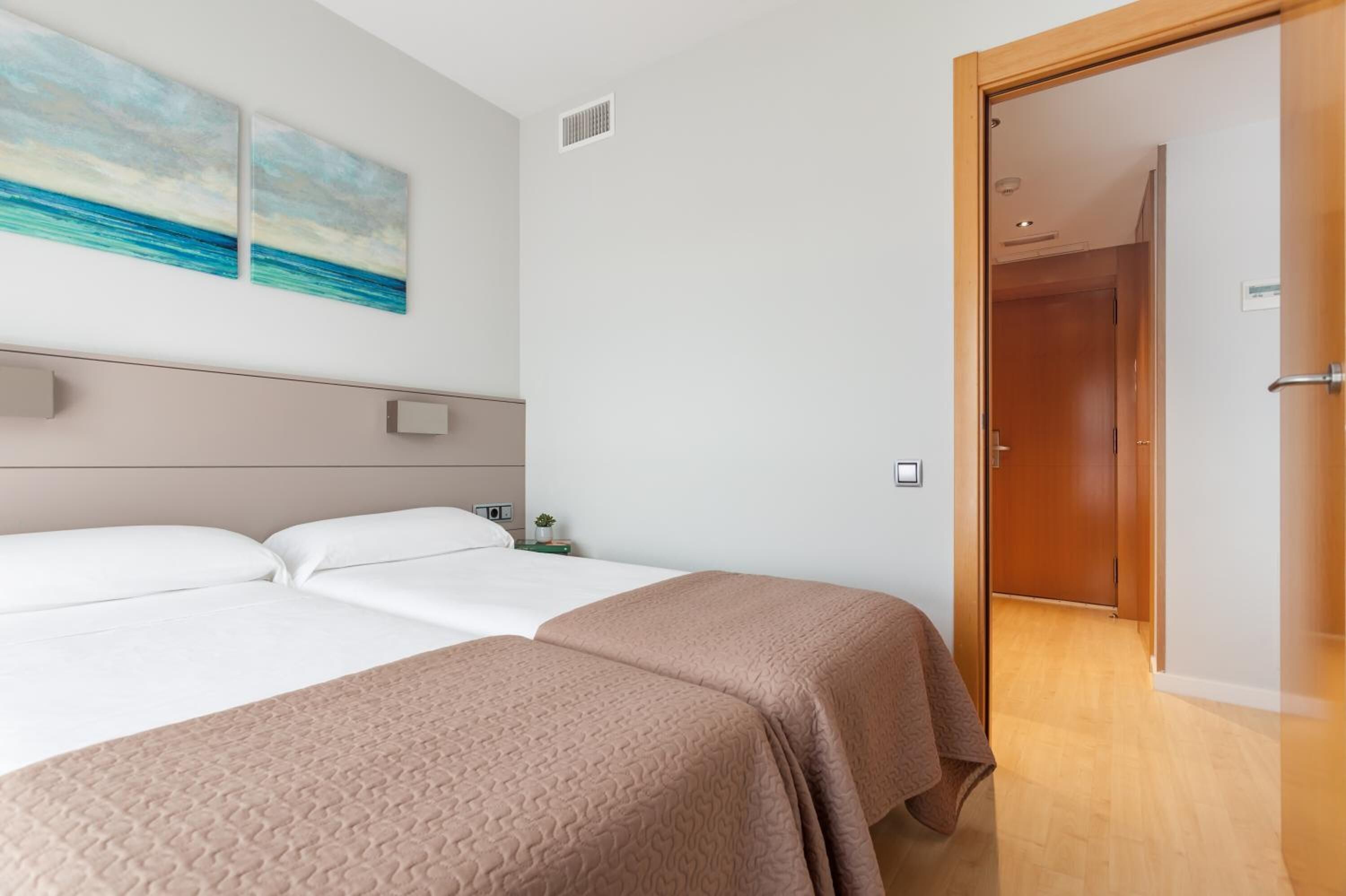 A hotel room with two beds, a wooden door, and a wall-mounted light fixture.