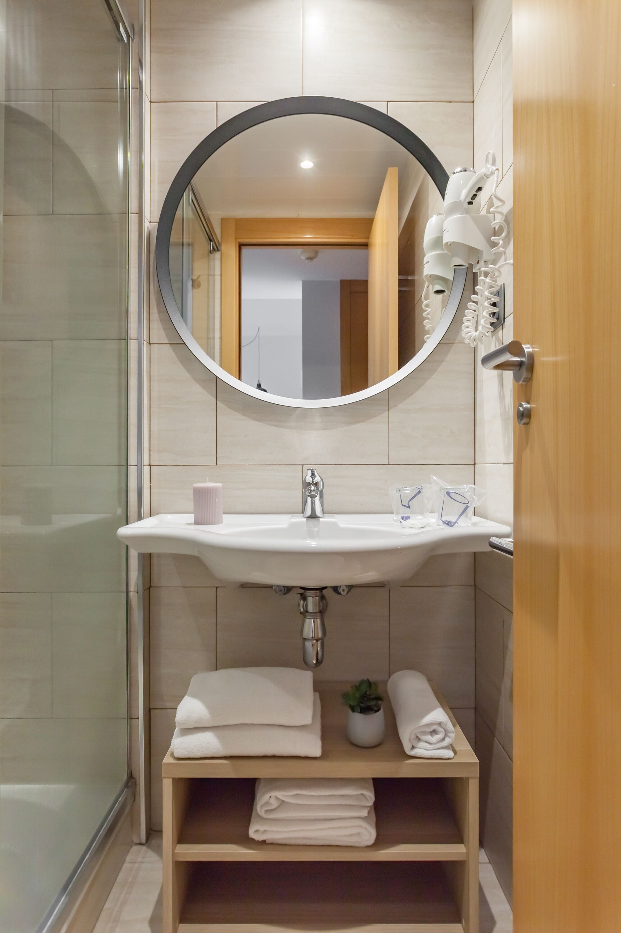 Un baño con un espejo redondo, un lavamanos blanco y un estante con toallas.