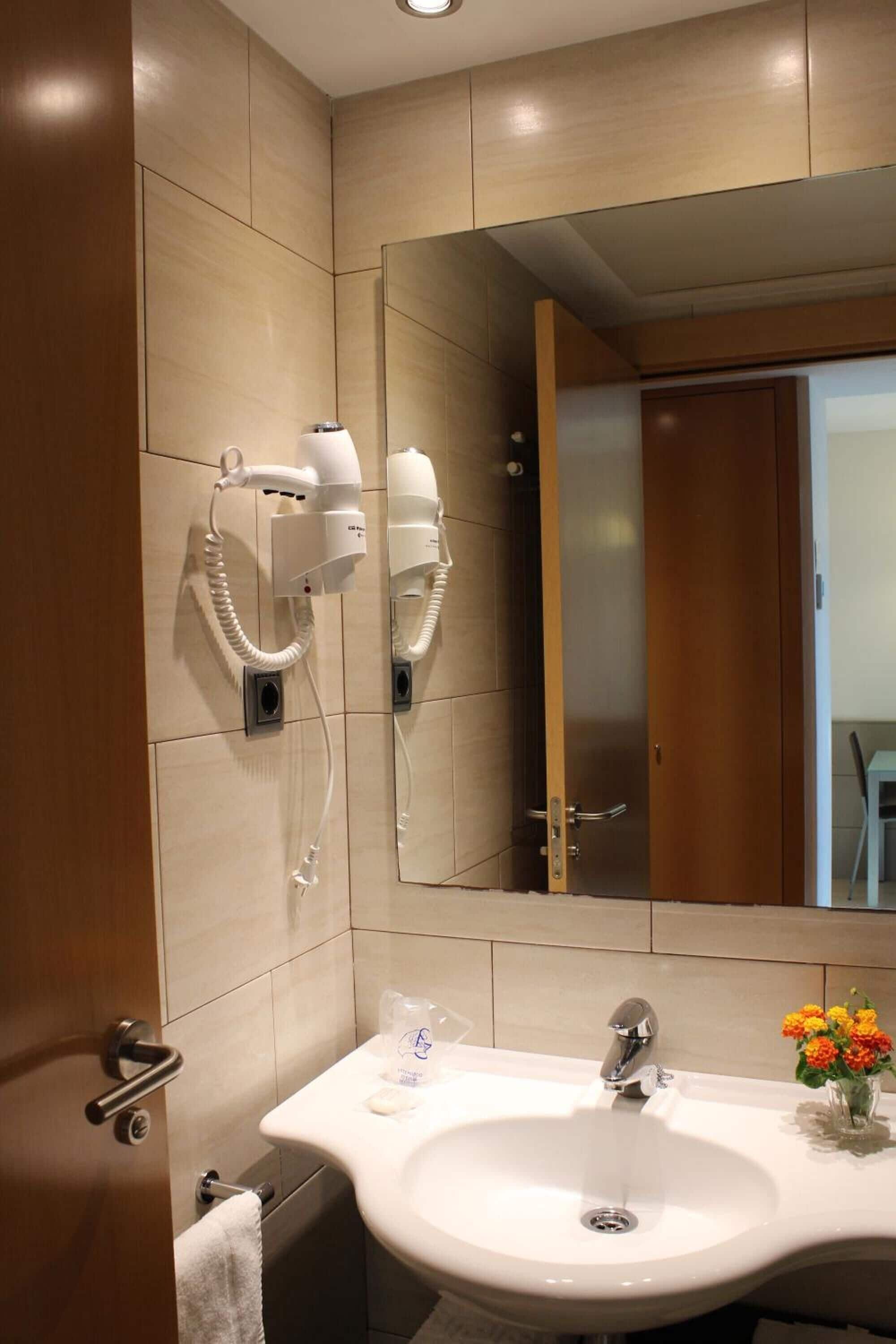 Un bany amb un mirall gran, dos assecadors de cabell, un lavabo i un ram de flors.