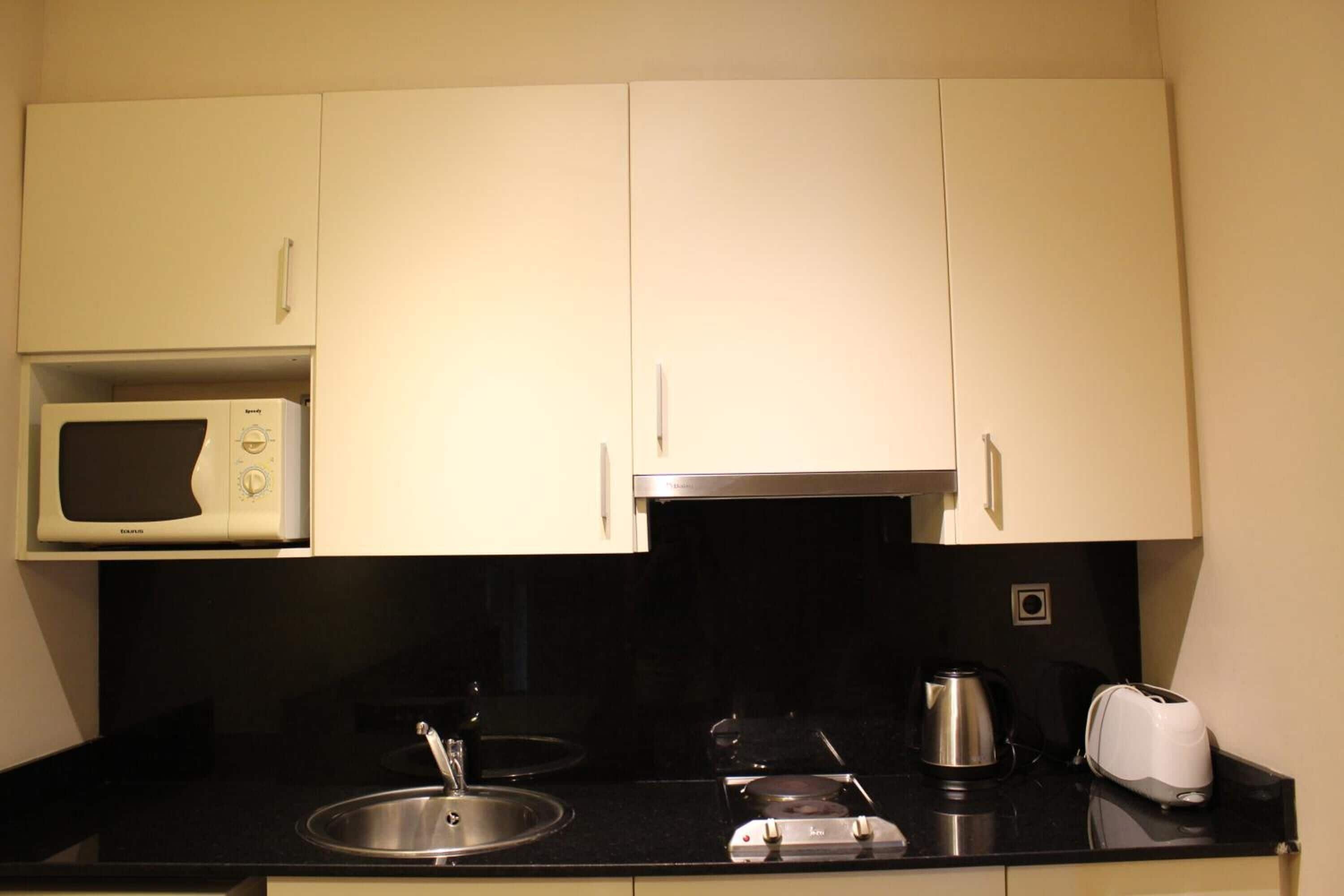 Una cucina compatta con microonde, fornello, bollitore e tostapane.